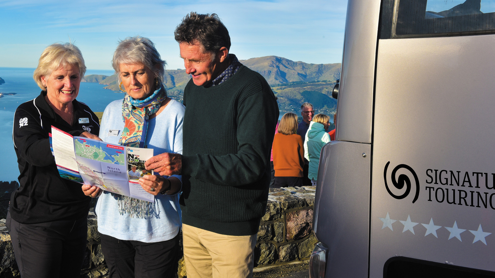 Three tourists checking out a map with a view of the ocean in the background