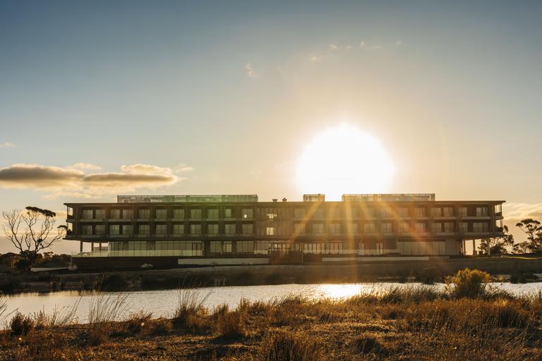 The sun sets in the sky behind the resort with a waterhole in the foreground