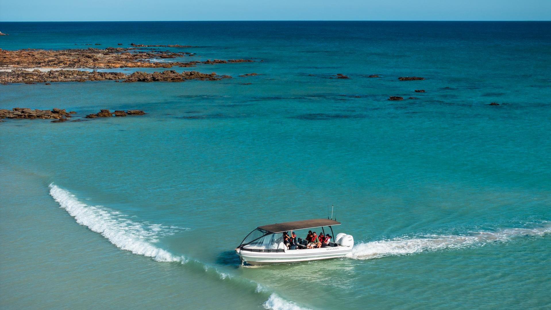 A small boat heads towards the shore across turquoise blue ocean