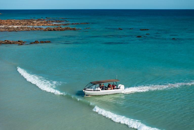 A small boat heads towards the shore across turquoise blue ocean