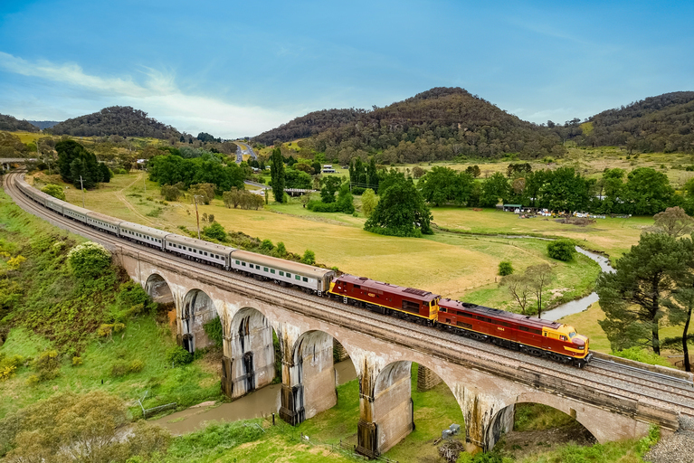 A train travels over a tall bridge with lush green hills in the background